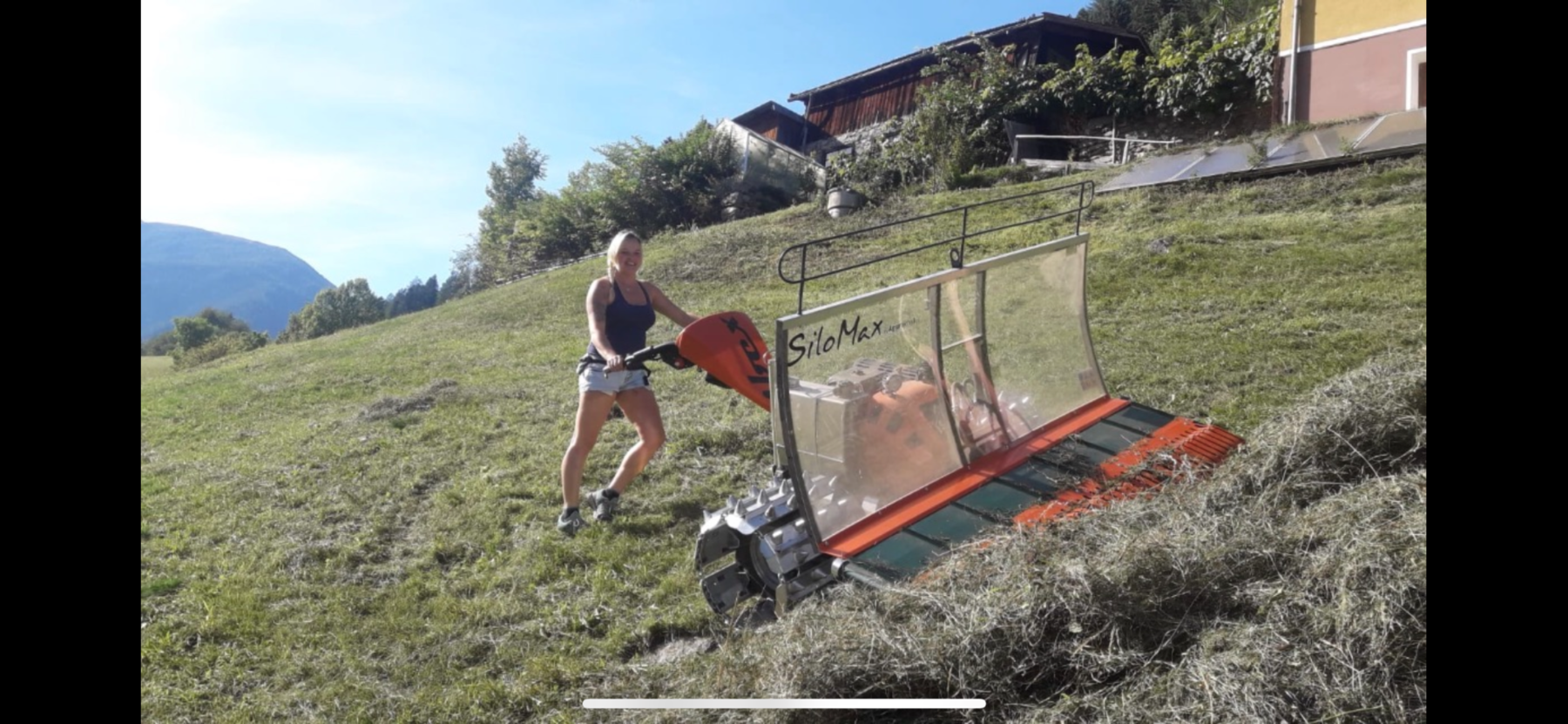 Eine Frau steht mit einem Mähgerät auf einer steilen Wiese