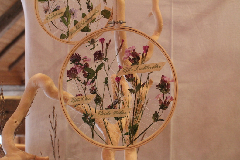 In einem runden Stickrahmen sind getrocknete rote Lichtnelken eingespannt.  In einem runden Stickrahmen sind getrocknete rote Lichtnelken eingespannt.