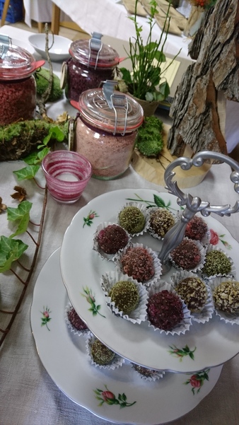 Auf einem dekorierten Tisch stehen Einmachgläser mit buntem Blütenzucker. Im Vordergrund selbstgemachte Pralinen. 