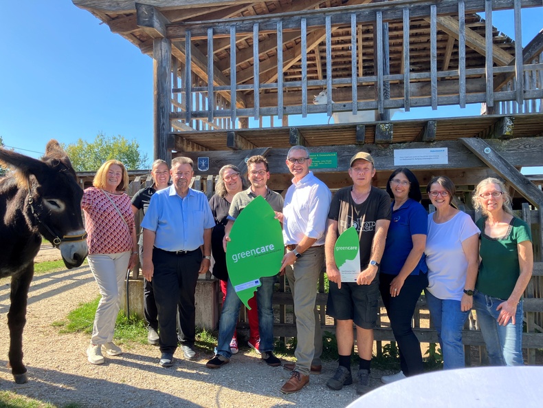 Einige Personen und ein Esel stehen im Halbkreis und halten eine Hoftafeln zur Kamera. Einige Personen und ein Esel stehen im Halbkreis und halten eine Hoftafeln zur Kamera.