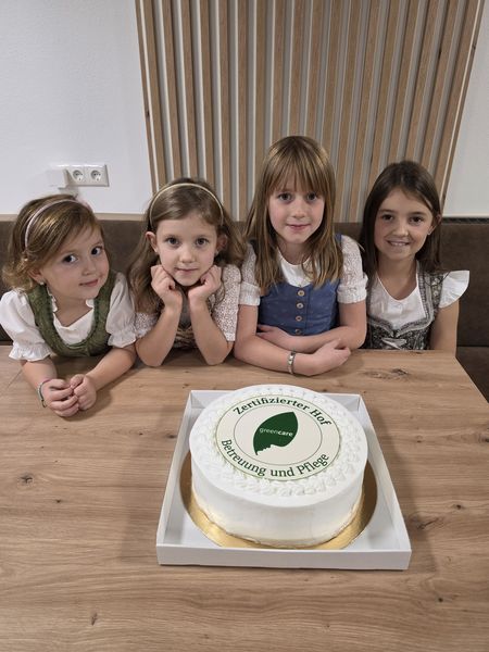 4 Mäderl vor einer Torte sitzend bei Tisch