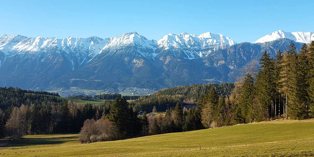 Landschaft mit Feldern, Wald und Bergen im Bezirk Innsbruck