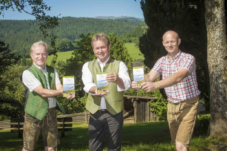 Drei Männer halten eine Broschüre über Almen in der Hand