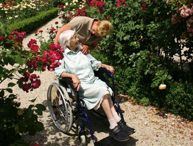 Ältere Frau wird im Rollstuhl durch den Garten geschoben Ältere Frau wird im Rollstuhl durch den Garten geschoben