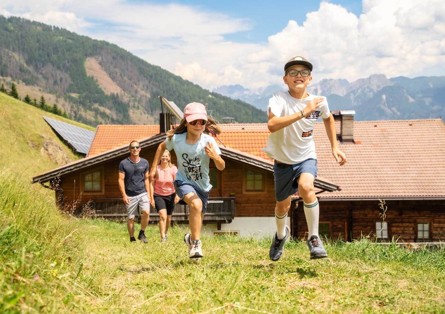 Kinder laufen auf einer Wiese im Hintergrund gehen die Eltern © TVB Osttirol